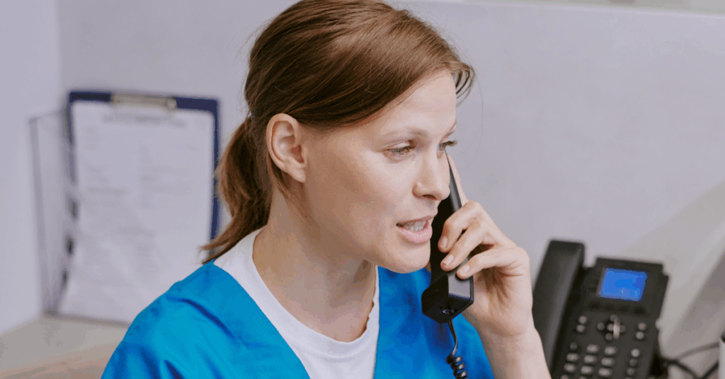 A look at how different businesses use phone systems for small businesses. A woman wearing scrubs is speaking on a corded phone in the office.
