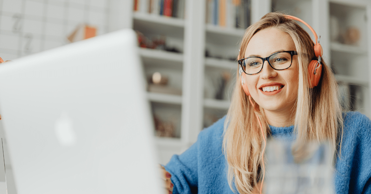 Woman smiles as she listens to headphones while using a laptop, likely thanks to consistent download speeds