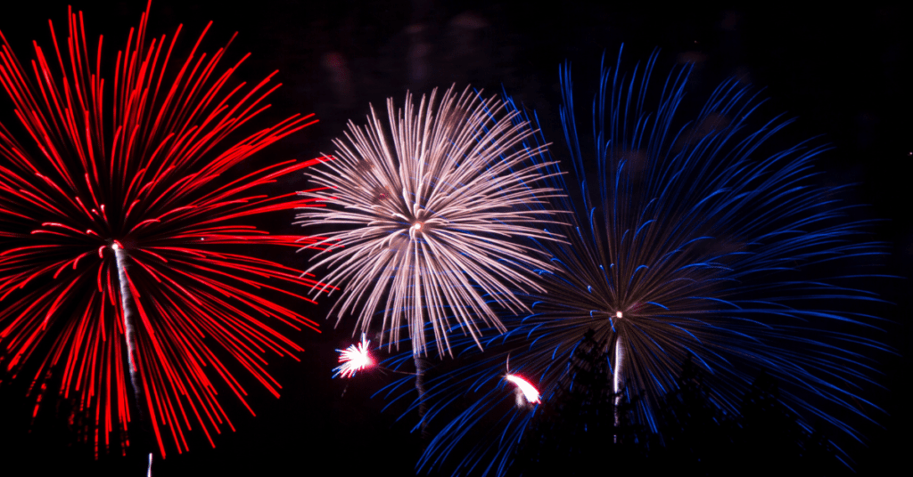 Fourth of July fireworks in the colors of red, white, and blue burst in the night sky.