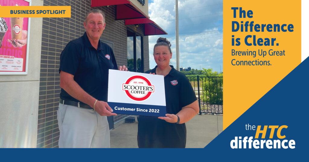 Owner and manager of Scooter's Coffee stand in front of the building holding a sign with their logo, plus the words "The Differens is Clear" and "Brewing Up Great Connections" along with the HTC difference logo