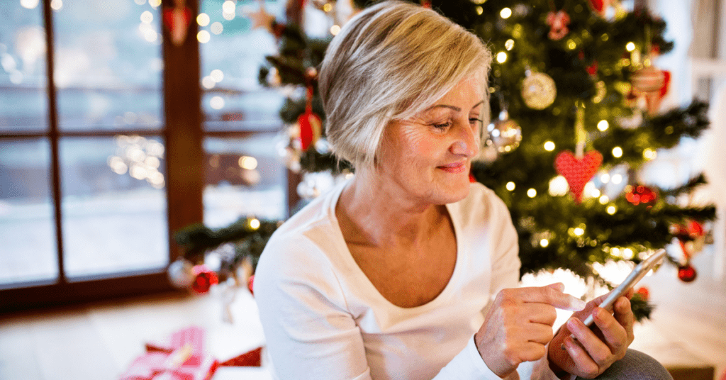 Woman watches phone in front of a Christmas tree during the holiday travel season