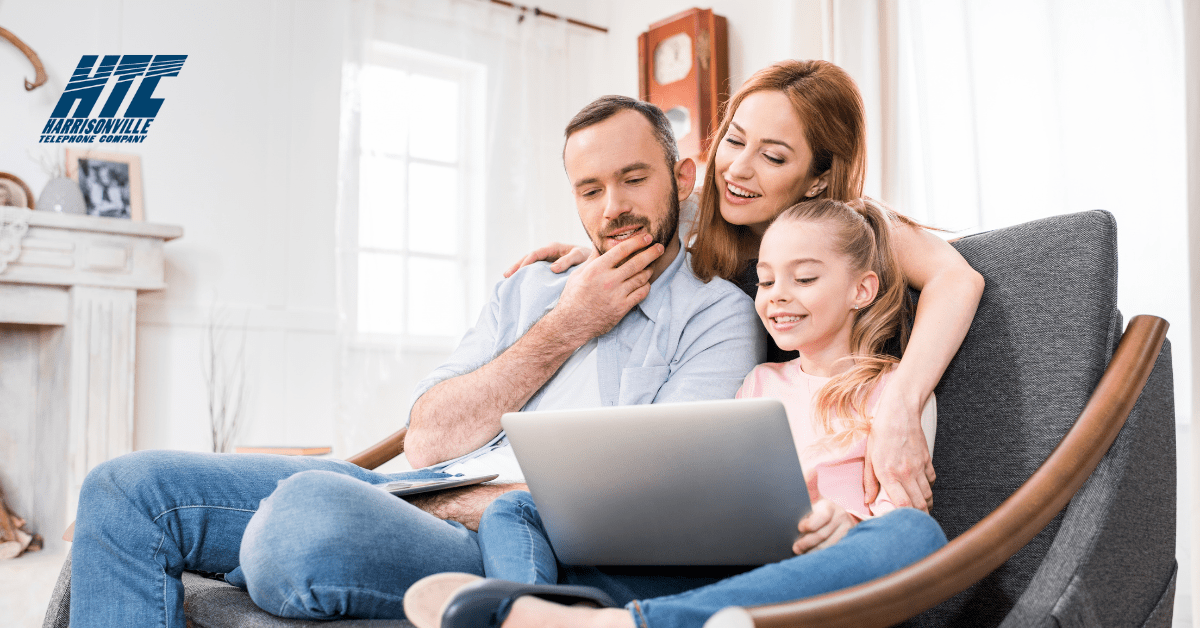 A family sits on a couch together while looking at a laptop thanks to home Internet bundles from HTC