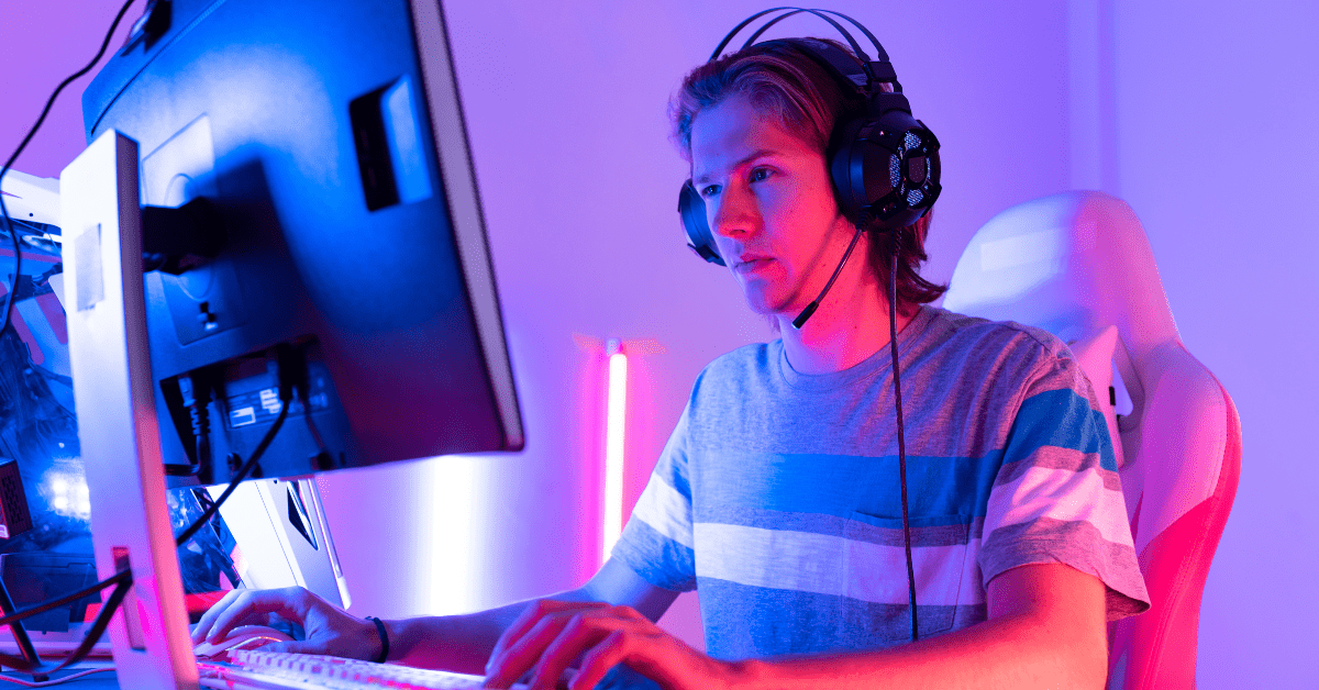 A young man sitting at a computer in a gaming chair, wearing a gaming headset, and looking for the best online gaming experience