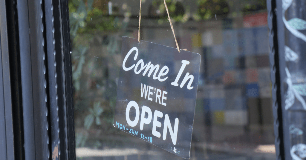 Header image for the blog titled "Why You Should Shop Local This Holiday Season" featuring a business' open sign that reads "Come In We're Open"