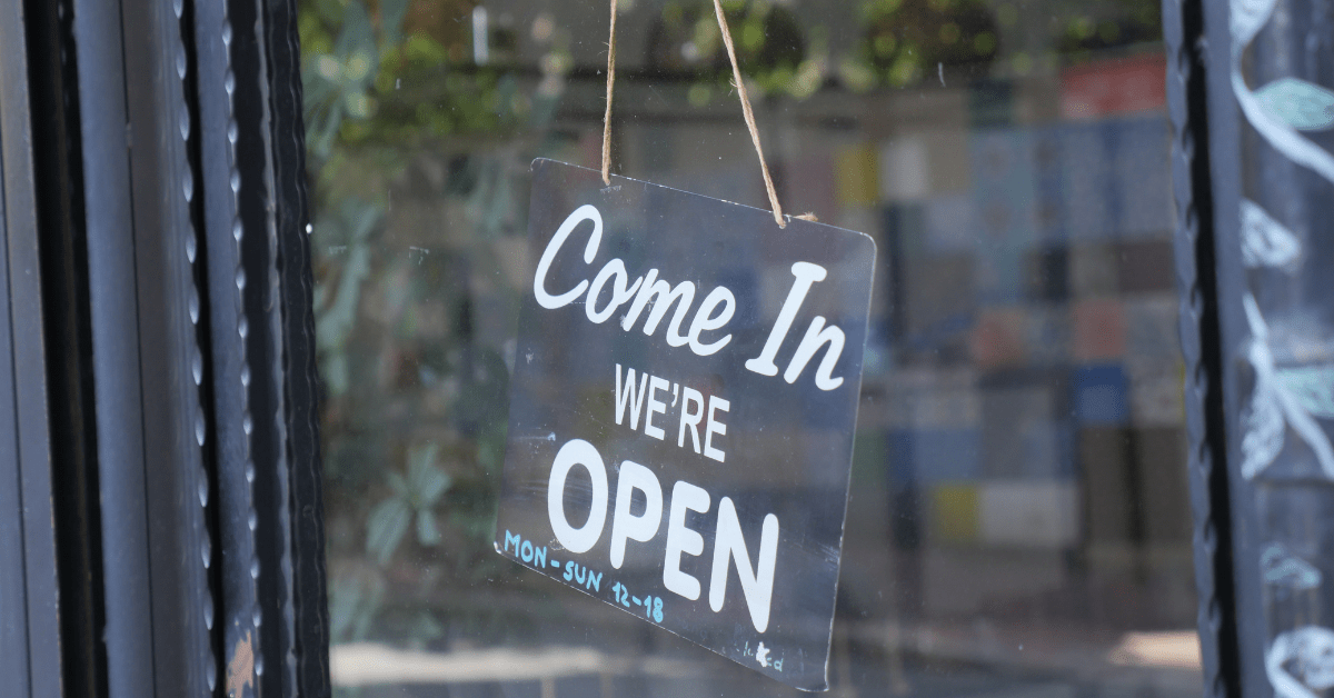 Header image for the blog titled "Why You Should Shop Local This Holiday Season" featuring a business' open sign that reads "Come In We're Open"