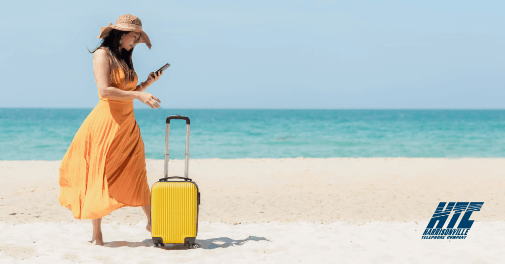Woman standing on a beach with a suitcase, checking in on her smart home while on vacation thanks to reliable Internet from HTC