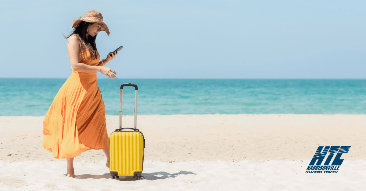 Woman standing on a beach with a suitcase, checking in on her smart home while on vacation thanks to reliable Internet from HTC